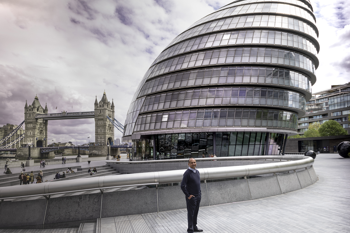 A man standing in front of Tower Bridge and the offices of the London Mayor.